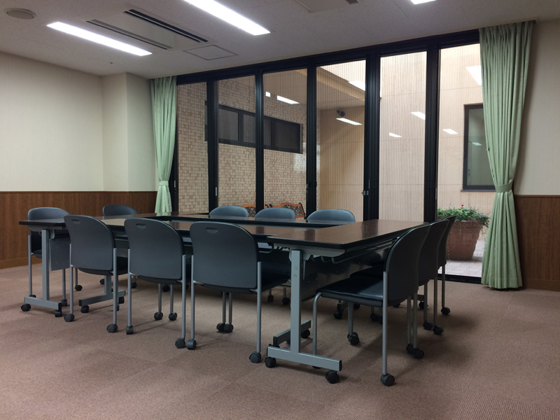 介護施設の会議室・多目的スペース。黒いテーブルと椅子が配置された広い共用部。