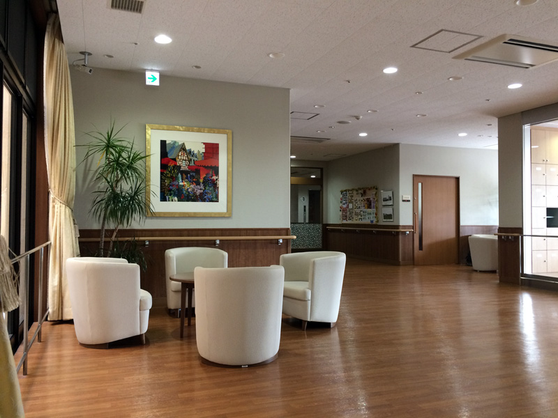 明るい共用スペース。円形のソファが配置され、観葉植物と装飾画が飾られている。